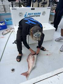 A young angler is preparing a large Snapper on the deck of the boat, showcasing the catch after a successful fishing trip.