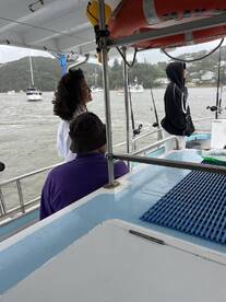 Two individuals are seated inside the boat, enjoying the view of the harbor with other boats in the background.