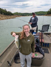 A young angler proudly displaying a large Largemouth Bass while fishing on a serene lake, accompanied by a fellow fisherman.
