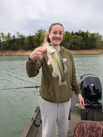 A young angler proudly displaying a large Largemouth Bass while fishing from a boat on a serene lake.