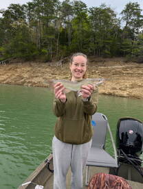 A young woman proudly displaying a freshly caught catfish while fishing from a boat in a serene lake setting.