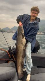 Angler proudly displaying a large catfish while fishing on a boat in a scenic lake environment.