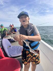 Excited young angler holding a small shark while fishing with friends on a boat, showcasing a fun day on the water.