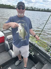 Angler proudly displaying a Crappie caught while fishing from a boat on a calm lake.