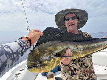 Angler proudly displaying a large Mahi Mahi while fishing offshore, showcasing a sunny day on the water.