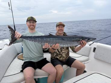 Two anglers proudly displaying a large Wahoo on a fishing boat during a deep-sea fishing trip.