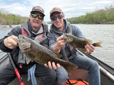 Two anglers proudly displaying their catch of smallmouth bass while fishing on a river.