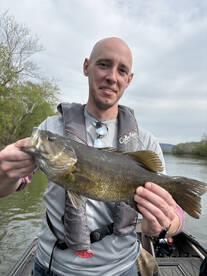 Angler proudly displaying a large Largemouth Bass while fishing on a river.