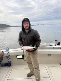 Angler proudly displaying a caught trout while fishing on a calm lake, showcasing a successful day on the water.