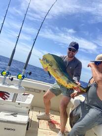 Two anglers proudly displaying a large Mahi Mahi aboard a fishing boat in open waters.