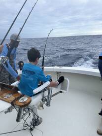 A young angler is seated in a fighting chair, engaged in reeling in a catch while fishing on a charter boat during a tournament.