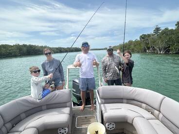 A family enjoying a fishing trip on a boat, with kids actively reeling in their catches in a scenic mangrove setting.