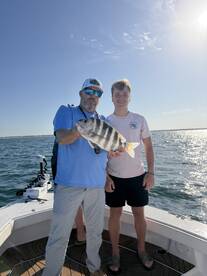 Two anglers proudly displaying a Sheepshead caught while fishing on a boat in clear waters.