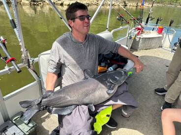 Angler holding a large Catfish while fishing on a boat, showcasing a successful catch during a day on the water.