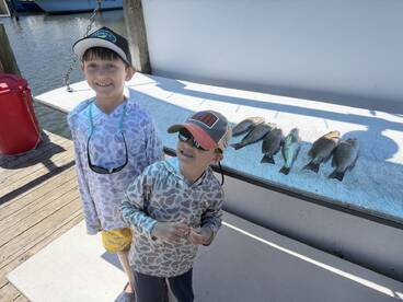 Two young anglers proudly posing next to their catch of several fish displayed on a cleaning table at the dock.