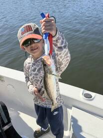A young angler proudly displaying a Speckled Trout while fishing on a boat.