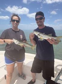 Two anglers proudly displaying their Snook catch while enjoying a sunny day on the water.