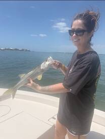 Angler proudly holding a Snook while fishing on a boat in sunny waters.
