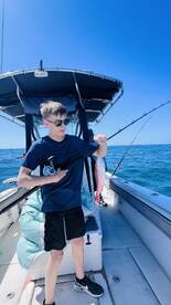 A young angler proudly displaying a freshly caught Snapper while fishing on a boat under clear blue skies.