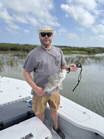 Angler proudly displaying a large Black Drum while fishing from a boat in a scenic coastal environment.