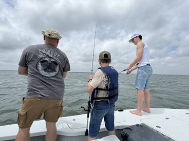 A family fishing trip in a coastal setting, featuring a young boy and two adults actively fishing from the boat.