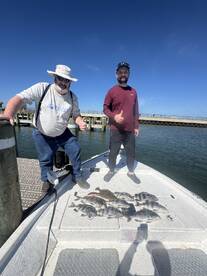 Two anglers proudly displaying their catch of various fish, including flounder and black drum, on the deck of a fishing boat.