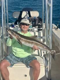 Angler proudly displaying a large Cobia while seated on a boat, showcasing a successful fishing trip.