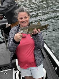 A happy angler proudly displaying a caught Smallmouth Bass while fishing on a boat.