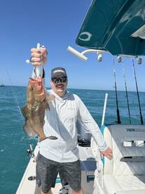 Angler proudly displaying a large Grouper while fishing on a sunny day, showcasing the excitement of a successful catch.