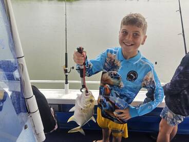 A young angler proudly displaying a Yellowtail Snapper while fishing on a boat, showcasing a vibrant fishing shirt and a joyful smile.