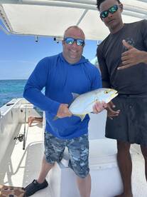 Two anglers proudly displaying a Yellowtail Snapper aboard a fishing boat in clear blue waters.
