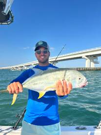 Angler proudly displaying a large Jack Crevalle while fishing near a bridge, showcasing a sunny day on the water.