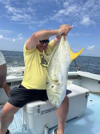 An angler proudly displaying a large Jack Crevalle while seated on a boat, enjoying a day of fishing in open waters.
