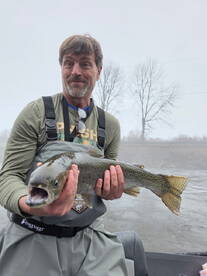 An angler proudly displaying a large Rainbow Trout while fishing on a foggy day, showcasing the excitement of a successful catch.