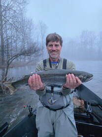 Angler proudly displaying a large Rainbow Trout while fishing in a foggy river setting.