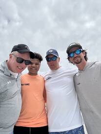 A group of four individuals posing together, likely after a fishing trip, with cloudy skies in the background.