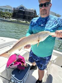 Angler proudly displaying a Redfish while fishing from a boat in a coastal area.