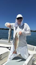 Angler proudly displaying a Speckled Trout and a Redfish while fishing on a sunny day.