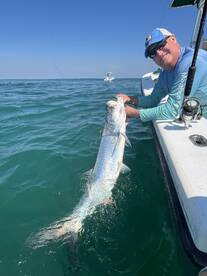 Angler reeling in a large Tarpon while fishing in clear waters, showcasing an exciting moment on the boat.