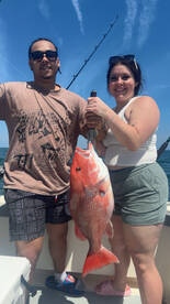 Two anglers proudly displaying a large Red Snapper while fishing on a sunny day.