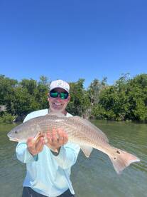 Angler proudly displaying a large Redfish while fishing in a scenic coastal environment.
