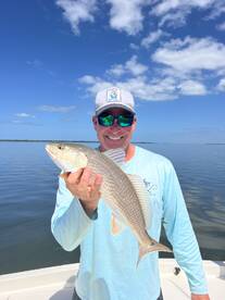 Angler proudly displaying a Redfish against a scenic backdrop of calm waters and blue skies.
