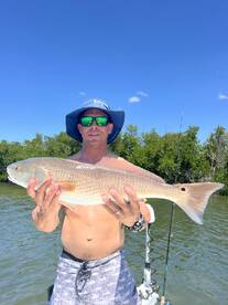 Angler proudly displaying a large Redfish while fishing in a scenic coastal environment.