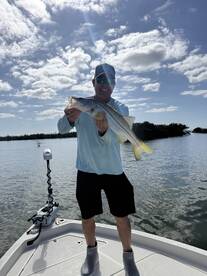 Angler proudly displaying a large Snook while fishing on a sunny day in a coastal waterway.