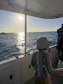 A young child enjoying a scenic view from inside the boat, with the sun setting over the ocean.
