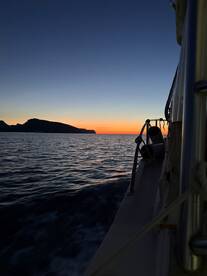 A serene sunset view from the side of a boat, showcasing the calm waters and distant land, perfect for a peaceful fishing experience.