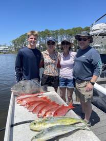 A family proudly displaying their catch of the day, featuring a variety of fish including a large grouper and several snapper, at a dockside location.