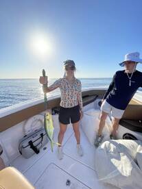 A young woman proudly displaying a Mahi Mahi on a boat during a sunny fishing trip.