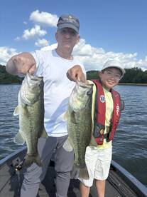 A proud moment on the water as a young angler and an adult display their impressive catch of two large Largemouth Bass while fishing together.