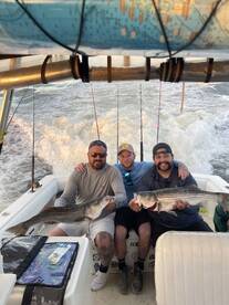 Three anglers proudly displaying their catch of striped bass while aboard a fishing boat, showcasing a successful day on the water.